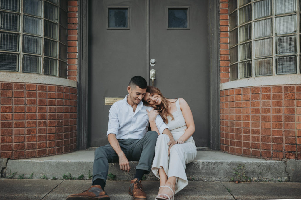 downtown memphis engagement session, a couple sits close together on an urban stoop with exposed brick. memphis, TN
