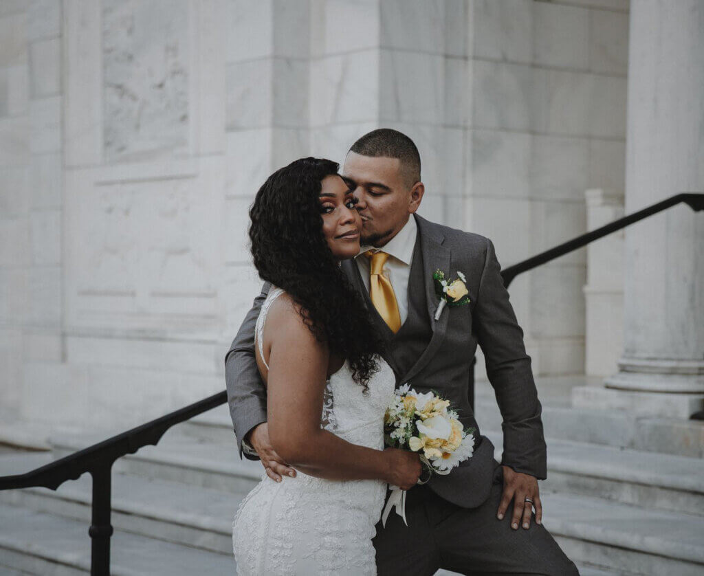 Groom kisses bride on the cheek on the steps of the Brooks Museum, photographed by Wandering Creative