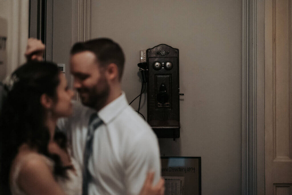 A couple stands together in an old hall of the Woodruff Fontaine House, with an antique phone in focus.