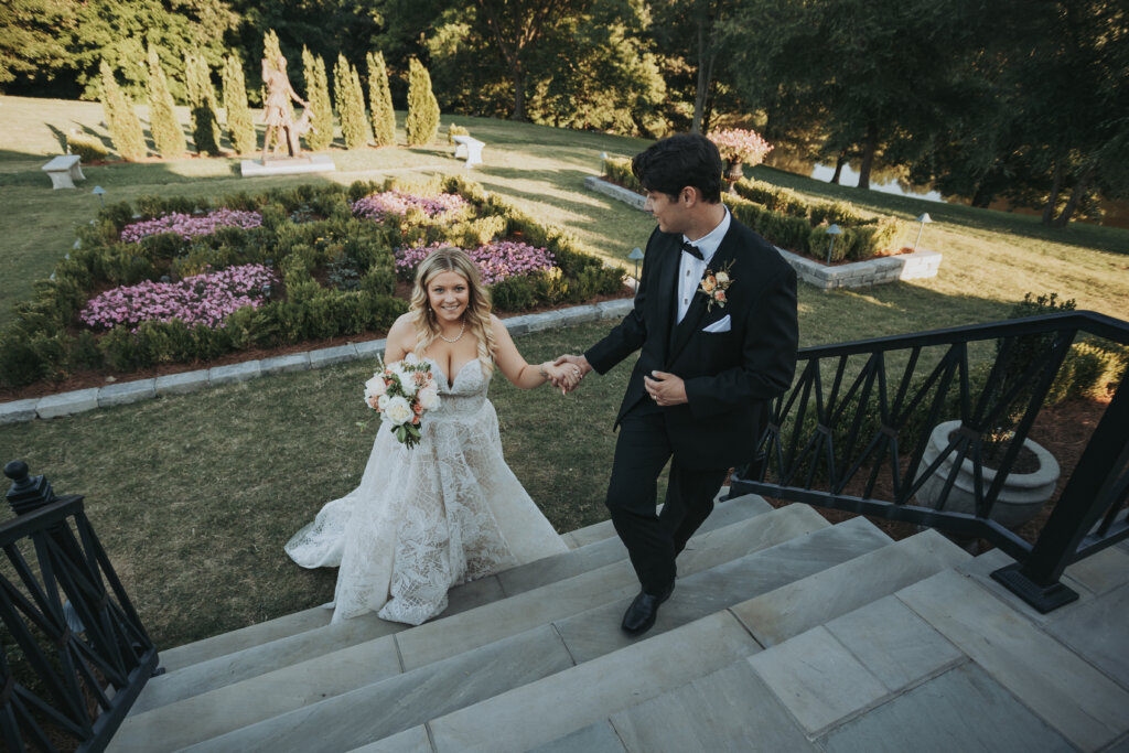 a couple walks up marble steps in a garden just after their wedding.