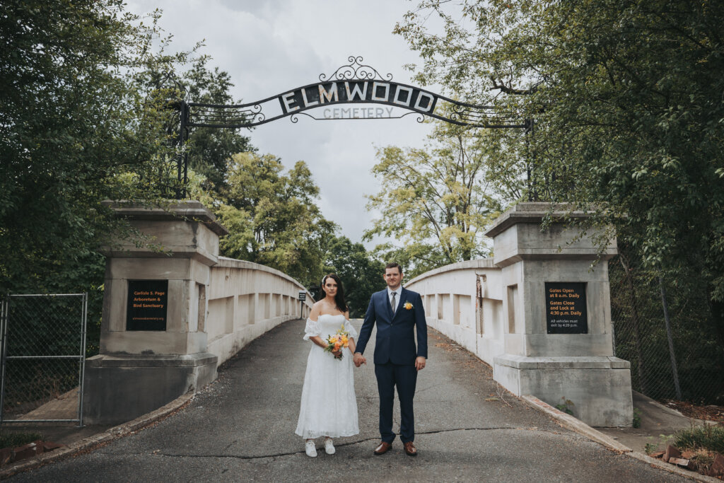 newlyweds stand under the Elmwood Cemetery Arch at the entrance to the venue.