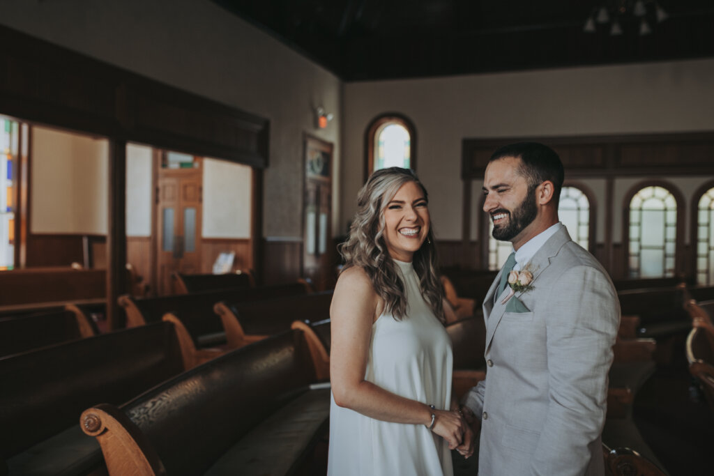a couple laughs together just after their first look inside of an empty church. Shot by wandering creative, elopement and travel photographer.