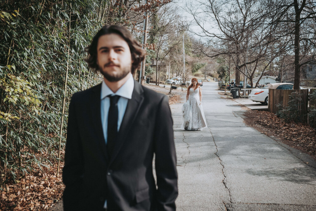 bride walks up behind groom during their first look in fayetteville, ar.