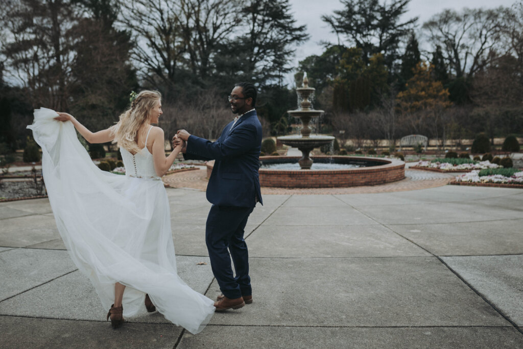 Newlywed couple dances together, spinning in front of the fountain in a Rose Garden.