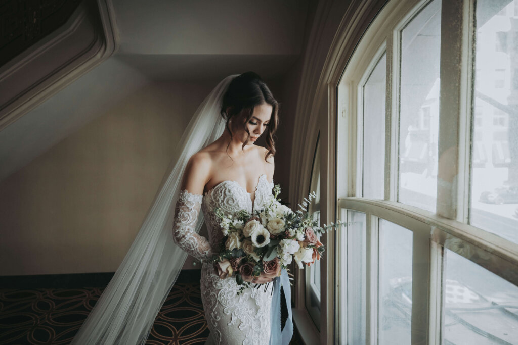 A bride gazes at her wedding bouquet by a window at the Seelbach Hotel in Louisville, KY.