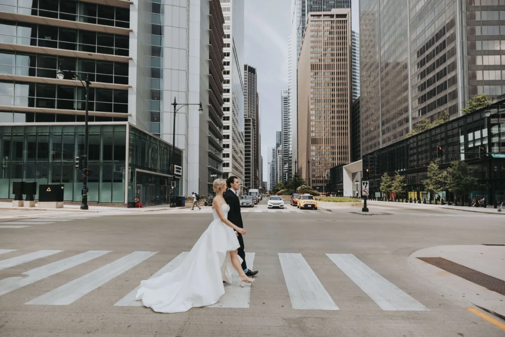 a wedding portrait in downtown chicago, of a couple crossing the street surrounded by buildings. 
